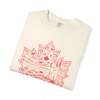 An off-white folded crewneck t-shirt featuring a red graphic of a Canadian maple leaf filled with illustrations of national parks, wildlife, and landmarks.